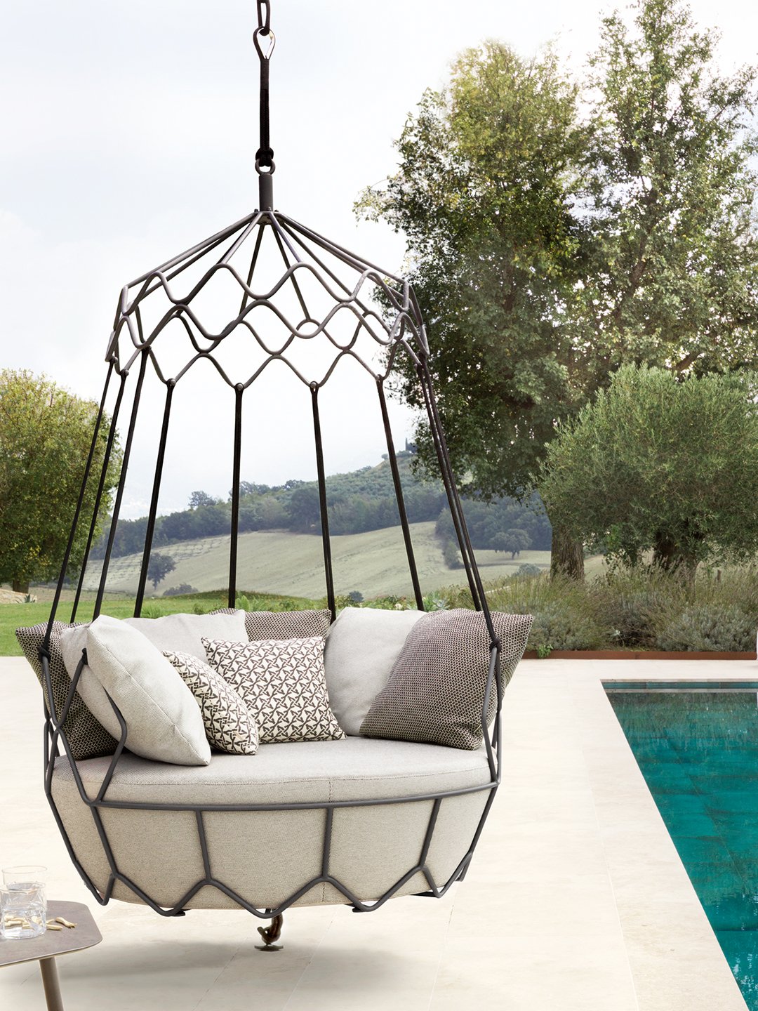 Round luxury hanging daybed with plush pillows in an swimming pool terrace.