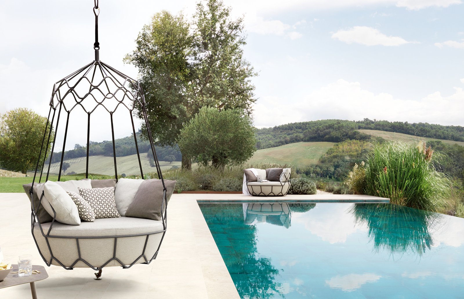Modern hanging daybed with metal frame by an infinity pool overlooking a scenic landscape.