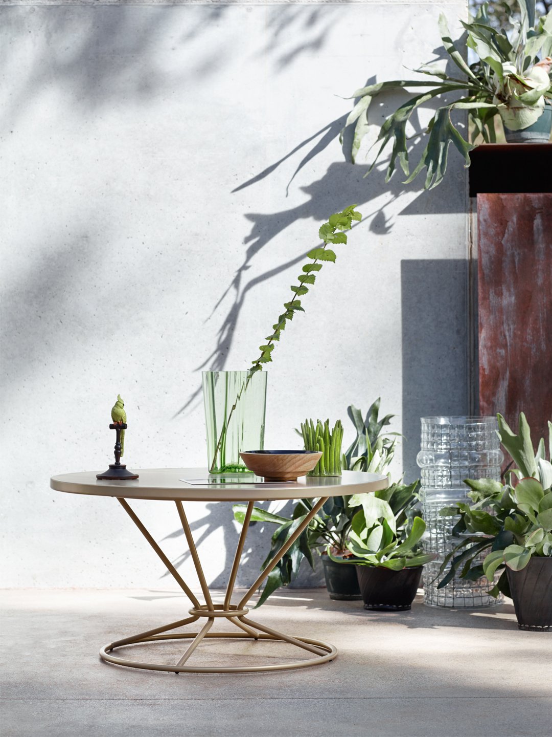 Round gold sculptural side table with a wireframe base and minimalist decor against a concrete wall with dramatic shadows.